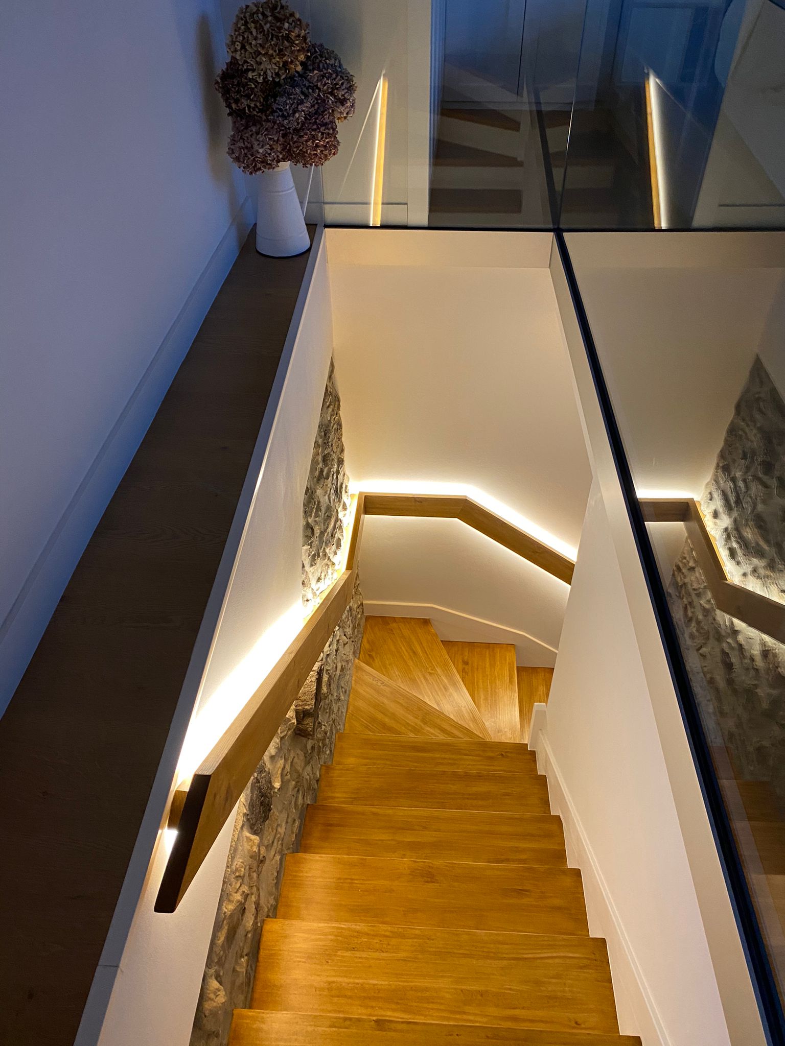 Escalera de madera con iluminación LED integrada en muro de piedra artesanal